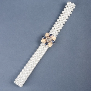 Close-up of white pearl belt with a gold floral buckle featuring blue gemstone accents