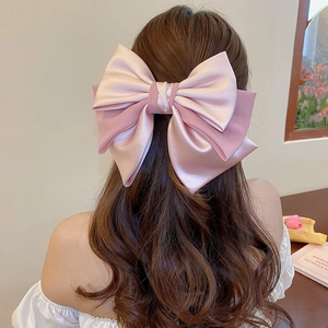 Detail of pink satin oversized bow hair clip worn by a model in a minimal setting