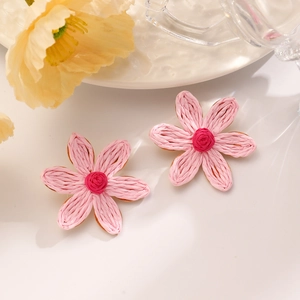 Detail of pink hand-woven raffia flower earrings on a white desk with floral decor