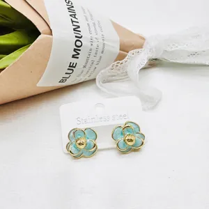 Elegant gold-rimmed light blue camellia studs on a stainless steel card display
