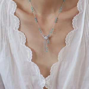 Detail of silver butterfly pendant necklace with blue beads and tassels on a model