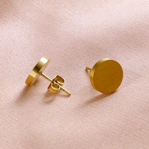 Pair of minimalist round gold stainless steel stud earrings on pink textured fabric