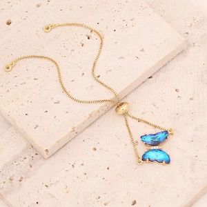 Close-up of golden butterfly charm with blue gradient crystal and adjustable slider clasp
