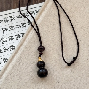 Macro detail of a dark wood gourd pendant with golden cap on a woven cord necklace