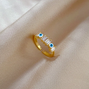 Detail of gold evil eye ring with blue enamel and rectangular zircon on silk background
