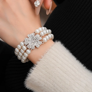 Close-up of multi-layer pearl bracelet with sparkling rhinestone clover clasp detail
