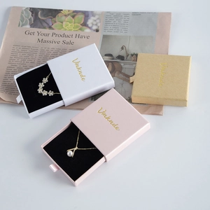 Detail of white, pink, and kraft paper drawer jewelry boxes with gold logo and foam inserts