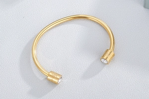 Close-up of golden cylinder cuff bracelet with engraved flower pattern and clear zircon