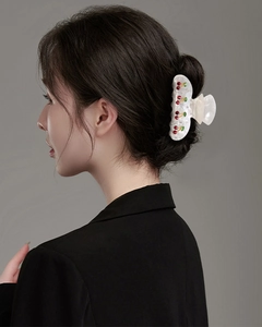 Detail of a white cherry claw clip with red rhinestones in a model's hair