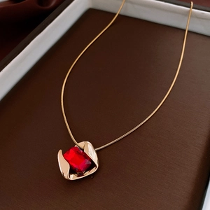 Detail shot of vintage gold chain with rhombic red gemstone pendant on leather tray