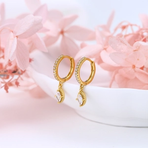 Elegant gold hoop earrings with marquise-cut crystal drops on a ceramic plate background