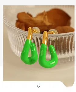 Nahaufnahme goldener U-Ohrringe mit grüner Emaille an einem strukturierten Glasrand