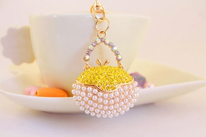 Detail of golden handbag keychain featuring yellow rhinestones and white faux pearls