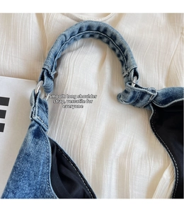 Detail of wide denim strap with silver metal ring on blue washed crossbody bag