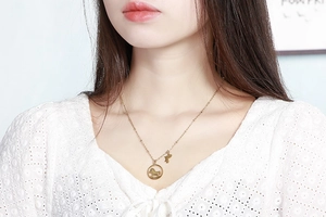 Gros plan d'un collier doré avec pendentif cheval et lettre H sur le cou d'un modèle