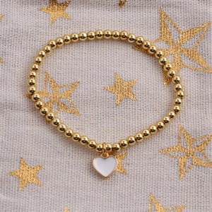 Detailed macro of gold bead stretch bracelet with white enamel heart charm on fabric