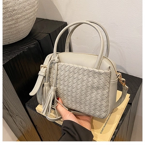 Detail of woven light gray handbag with tassel pendant and detachable strap