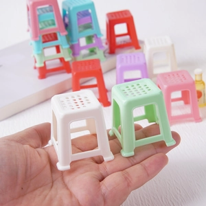Miniature dollhouse plastic stool models in various colors held in hand for scale