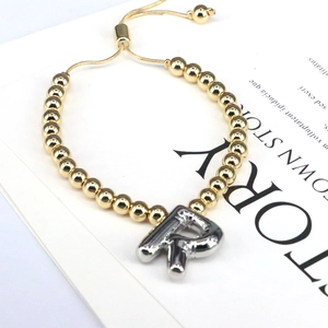 Detailed shot of golden bead bracelet with silver balloon letter R charm and adjustable clasp