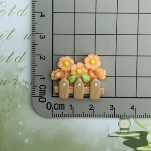 Macro shot of an orange resin flower on a fence accessory measured on a ruler scale
