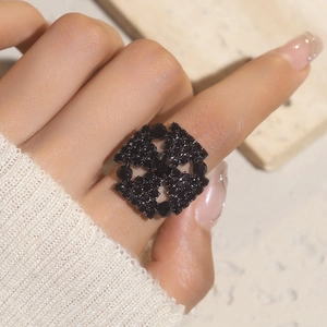 Close-up of a bold black rhinestone ring in a hollow geometric floral pattern on a finger
