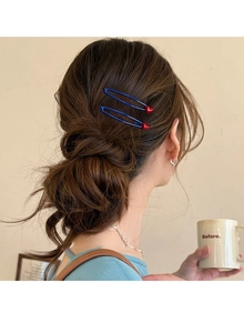Detail view of two blue bobby pins with red 3D heart accents in a braided hairstyle