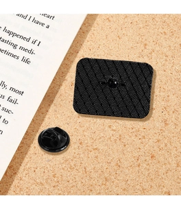 Detail view of a black metal pin back with textured surface and rubber clutch on cork