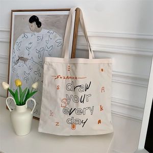 Close-up of beige canvas tote bag with artistic typography and vibrant orange letter prints