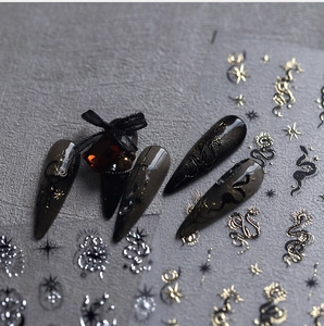 Macro shot of dark Gothic nail stickers with gold sun moon and snake totem patterns