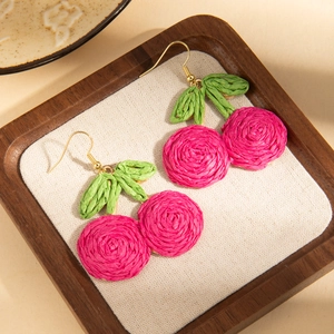 Macro shot of handmade woven cherry earrings with green leaves and gold hooks