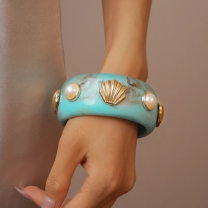 Detail view of turquoise resin cuff bracelet with gold shell and pearl embellishments