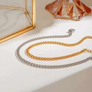 Two-tone gold and silver double Cuban link anklets displayed on a white luxury surface