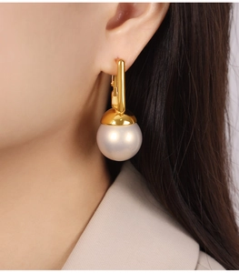 Gros plan de boucles d'oreilles dorées avec perles satinées portées par un mannequin