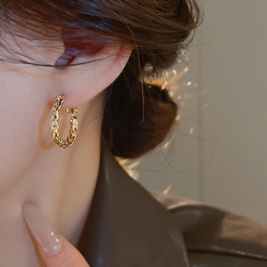 Close-up of golden twisted hoop earrings on a model showing refined metal texture
