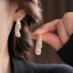Close-up of golden streamlined earrings featuring paved cubic zirconia on a model