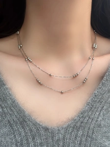 Close-up of double-layer beaded silver necklace on a grey sweater for layering style