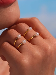 Close-up of four stacked gold rings with white pearls and diamonds on a model's hand