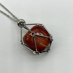 Detail of a natural red stone pendant inside a silver stainless steel mesh net cage