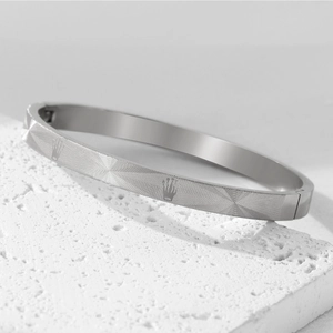 Detail showing radial textured surface and crown logo on silver stainless steel bangle