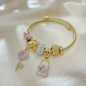 Close-up of golden beaded bracelet with pink crystal, key and heart lock charms on satin