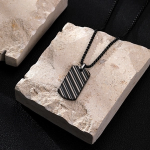 Men's black titanium steel dog tag necklace with textured stripes on a stone base