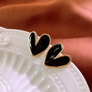 Close-up of black heart earrings with gold trim on white porcelain and silk fabric