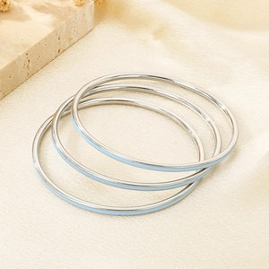 Detail of three stackable stainless steel bangles with light blue enamel on fabric background