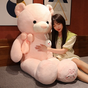 Detail of giant pink teddy bear with plush texture, satin bow, and bunny embroidery