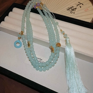 Close-up of light blue glass prayer beads necklace with silk tassel and golden cloud charms