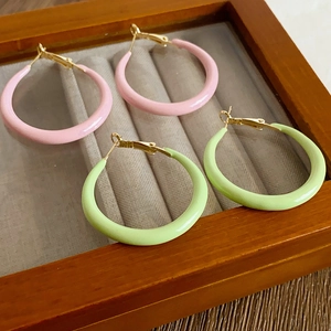 Macro detail of pink and green enamel hoop earrings in a wooden jewelry display case