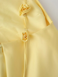 Close-up of yellow satin dress featuring 3D flower applique and metal strap buckle