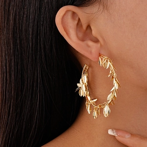 Close-up of golden metallic leaf hoop earrings worn on ear with professional soft lighting