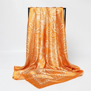 Détail du foulard carré en satin orange à motif cachemire drapé sur un support noir
