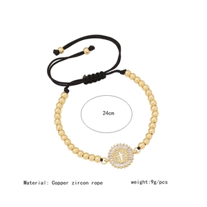 Detail view of gold beaded bracelet with zircon cross charm and adjustable rope